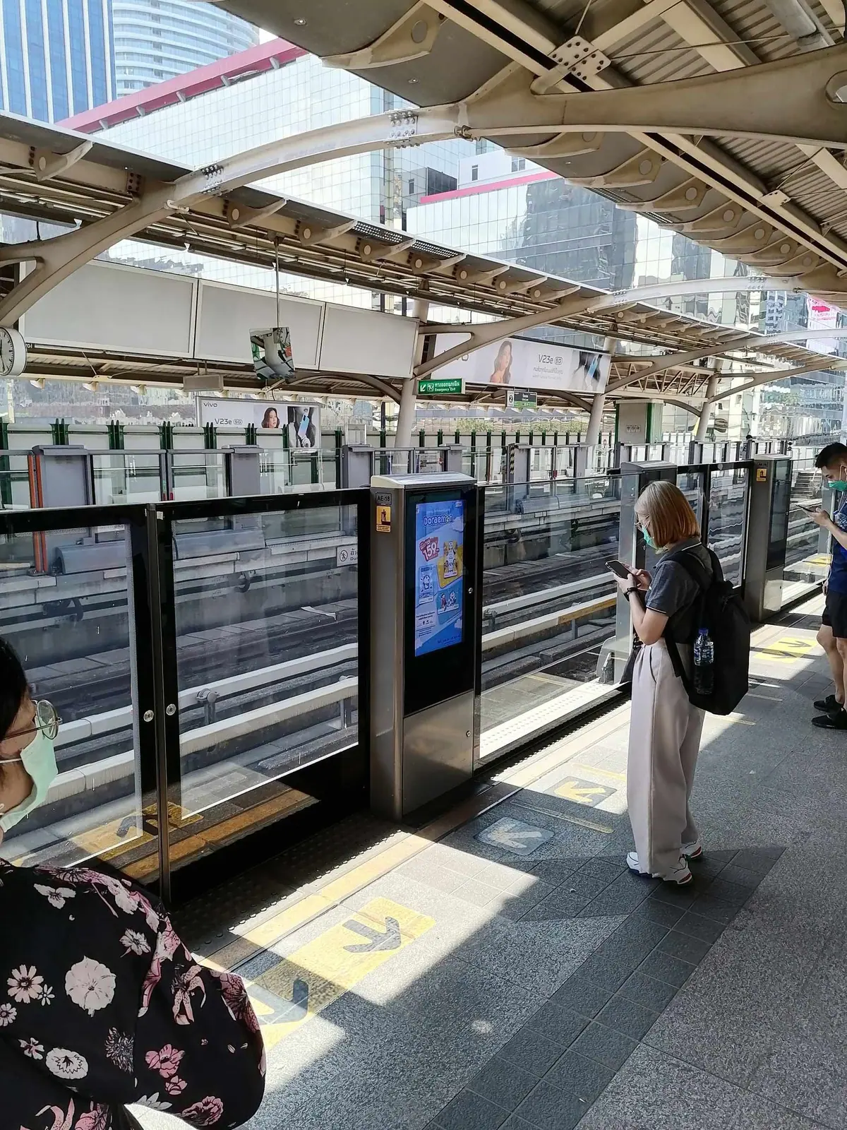 BTS Skytrain platform in Bangkok, passengers looking at their phones