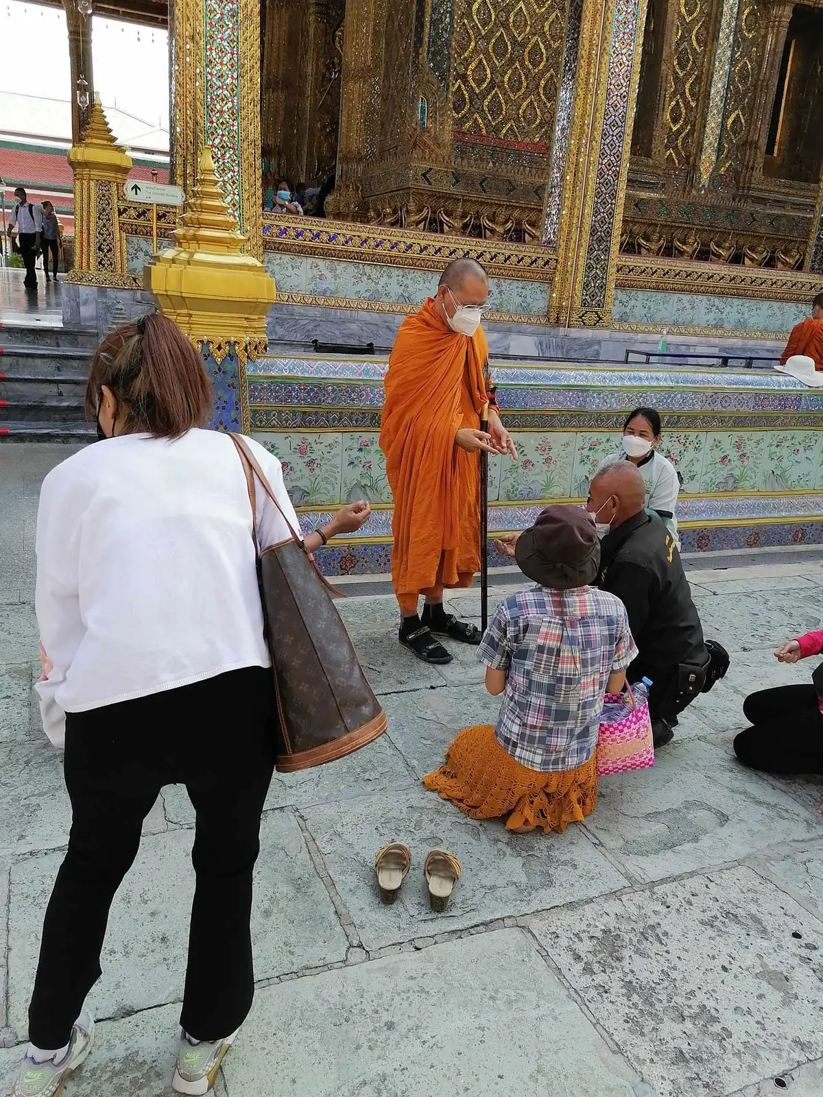 Monk at Wat Phra Kaew blessing worshippers and tying sai sin strings on their wrists